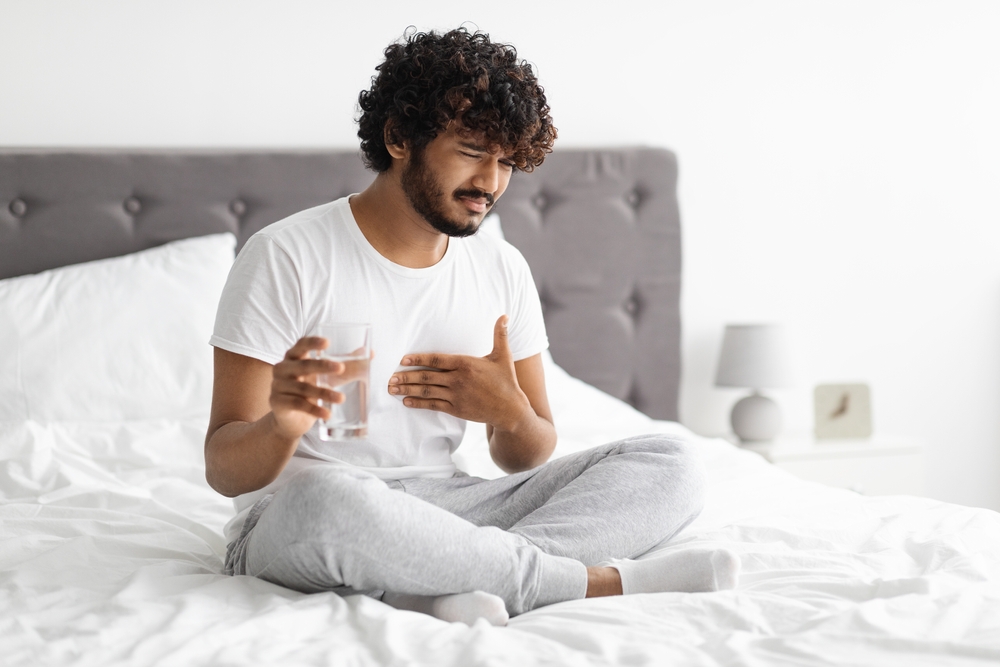 man with acid reflux sitting in bed with a hand over his chest